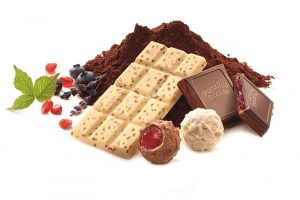 Eine Mischung aus Schokoladenstücken, Tafeln und Pralinen mit Kakaopulver im Hintergrund. Dekoriert mit Granatapfelkernen, Heidelbeeren und Minze.