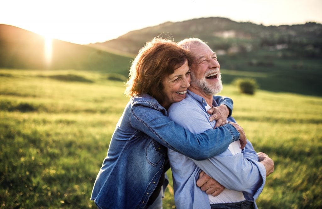 Happy looking elderly couple in an embrace. Nature in the background.