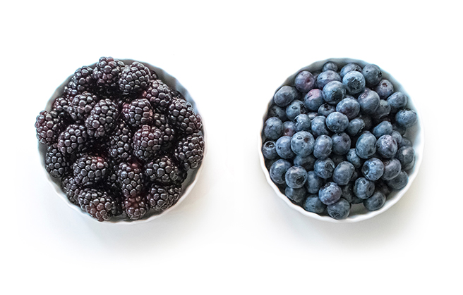 A bowl of fresh blackberries next to a bowl of fresh blueberries.